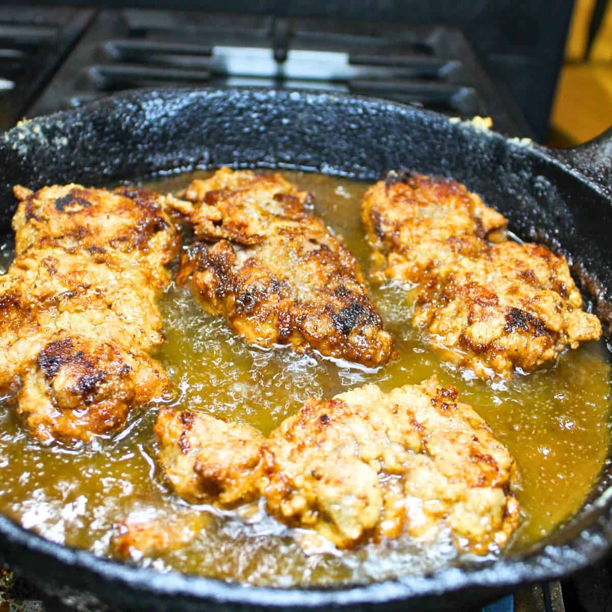 A cast-iron skillet cooking cube steak until golden brown.