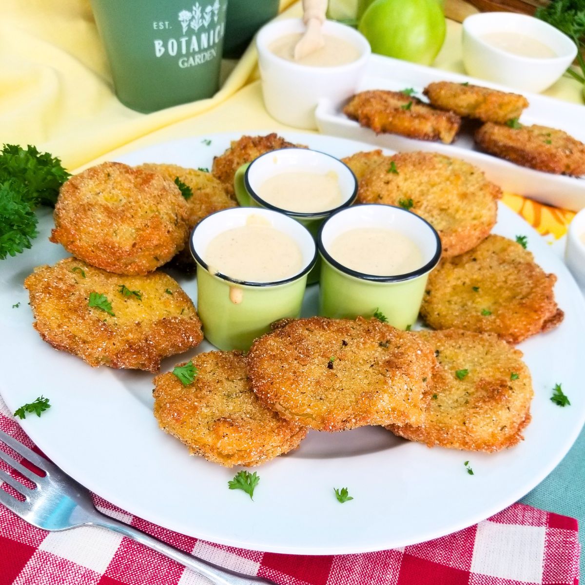 Fried Green Tomatoes on a white plate, a red and white napkin, fork, and green bowls with dipping sauce.
