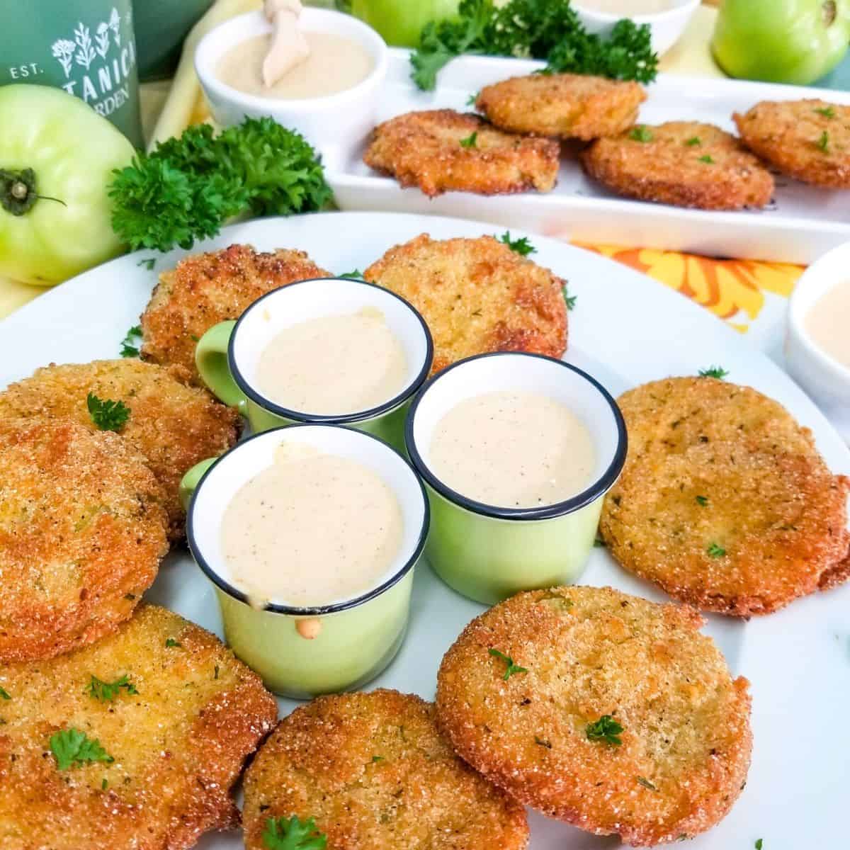 The finished recipe of fried green tomatoes on a white plate and remoulade sauce in small green bowls.