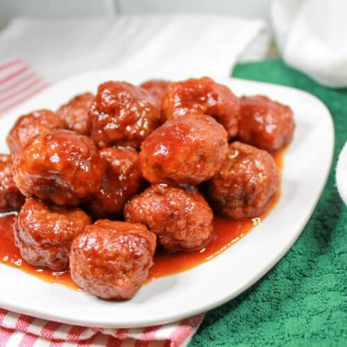 Meatballs on a white plate with a green and red and white dish towel under the plate.