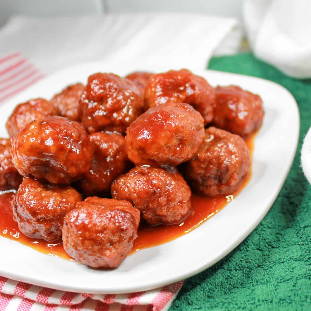 Meatballs on a white plate with a green and red and white dish towel under the plate.