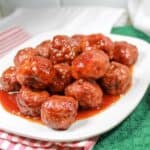 Meatballs with grape jelly sauce on a white plate. Green and white dishtowels under the plate.
