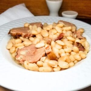 Great Northern Beans with pork chop pieces in a white bowl sitting on a table.