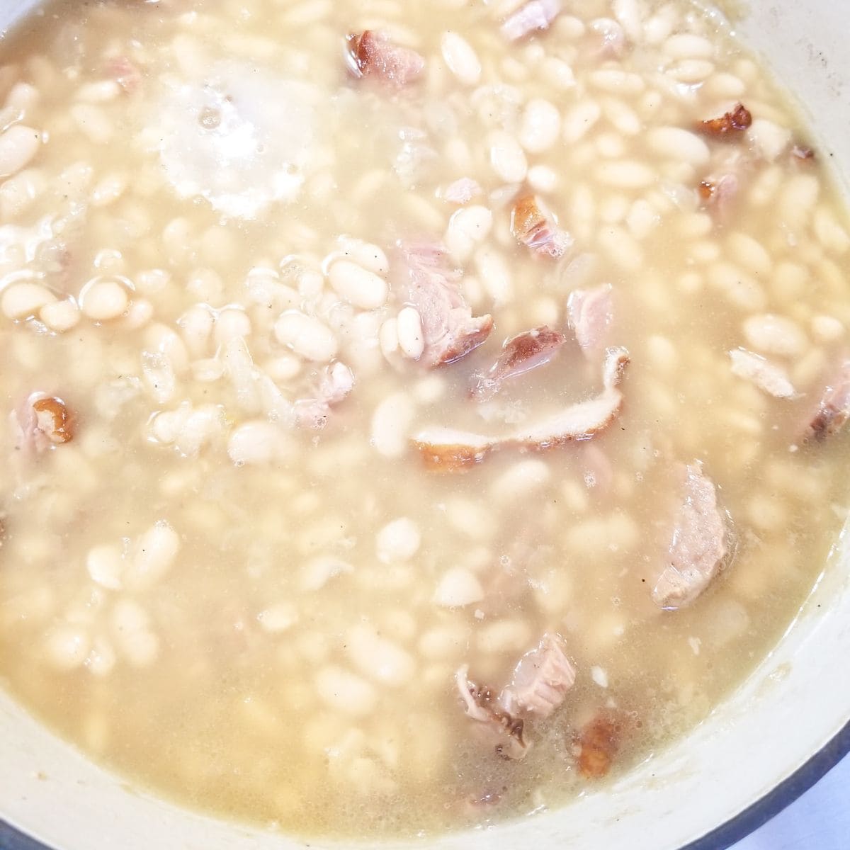 Creamy Great Northern beans simmering slowly with smoked meat in Dutch oven.