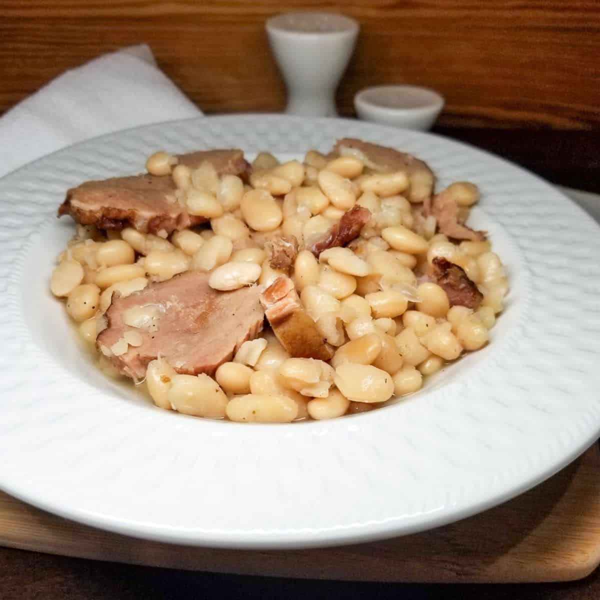 Close-up of tender Great Northern beans showing creamy texture after cooking. Served in a white bowl with smoky meat.