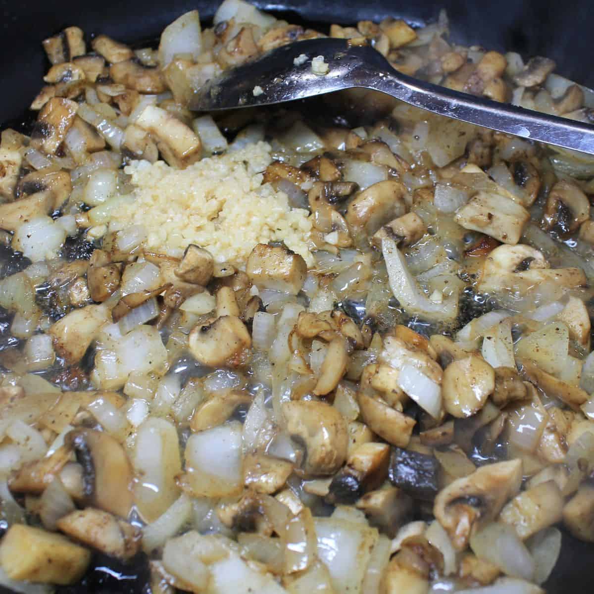 Onions, mushrooms, and garlic in a skillet with a spoon.