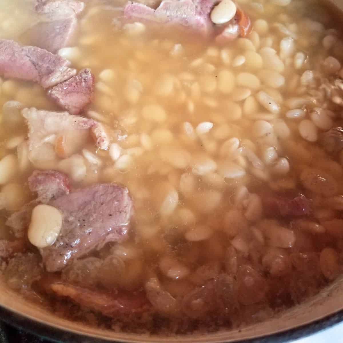Big pot of ham and beans simmering with dried lima beans and smoky ham on the stove.