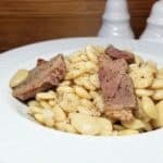 Bowl of old-fashioned ham and beans served hot with pieces on ham on top. Served in a white bowl with salt and pepper.