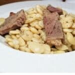 Ham and beans served in white bowl on farmhouse table.