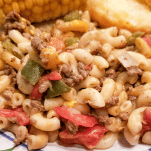 Hamburger noodle casserole on a plate with corn and bread.