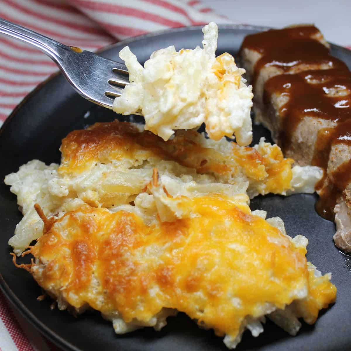 Hash Brown Casserole with a fork on a black plate with bbq.