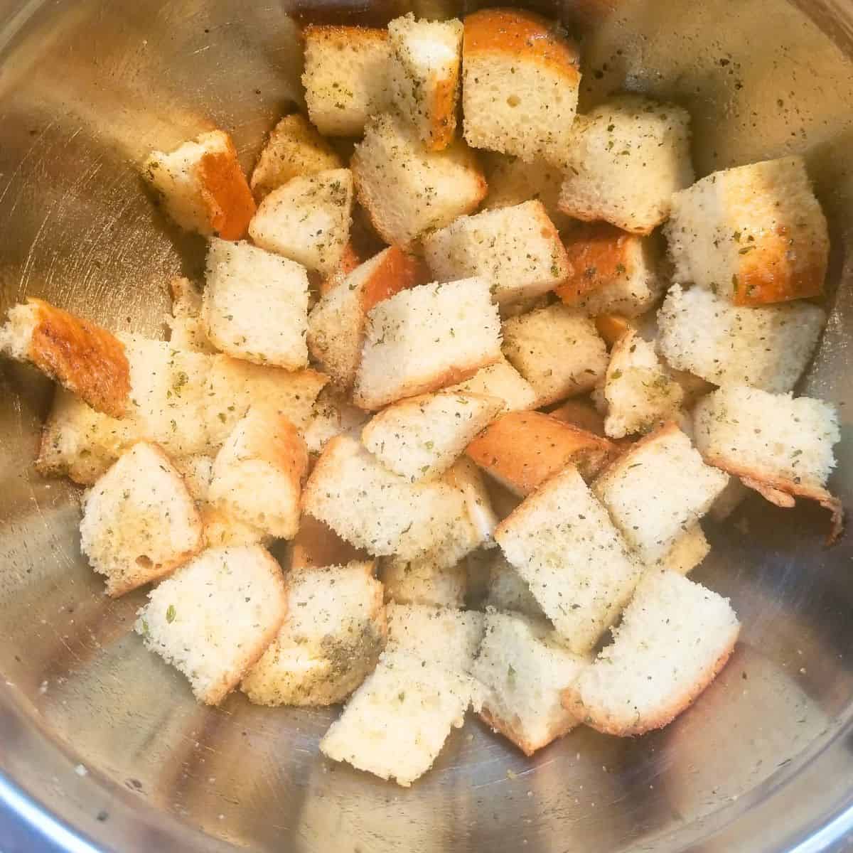 Bread cubes in a bowl with oil and seasonings mixed in.