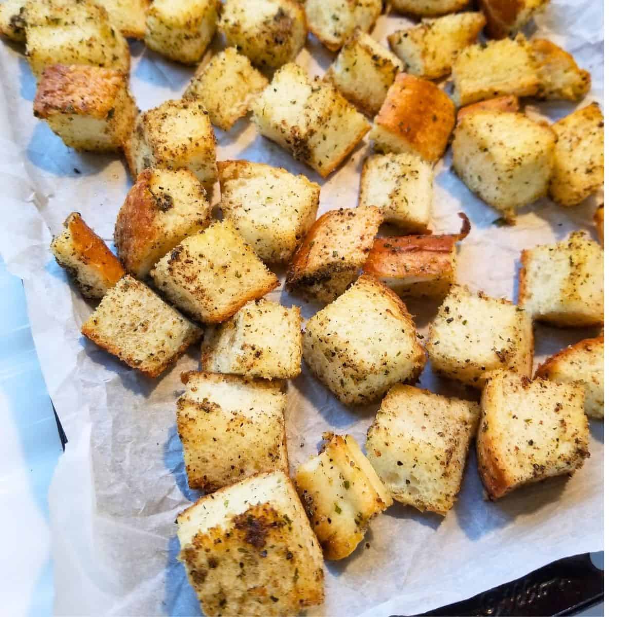 Baked croutons on a parchment paper lined baking sheet.