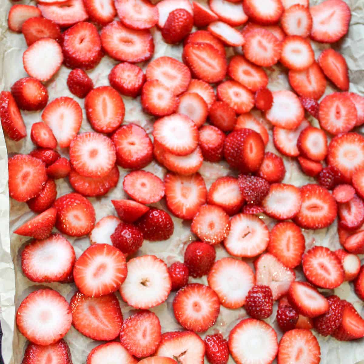 Sliced strawberries on a parchment paper lined baking sheet.