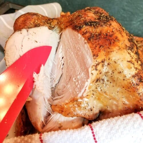 A cooked turkey sliced with a red knife.