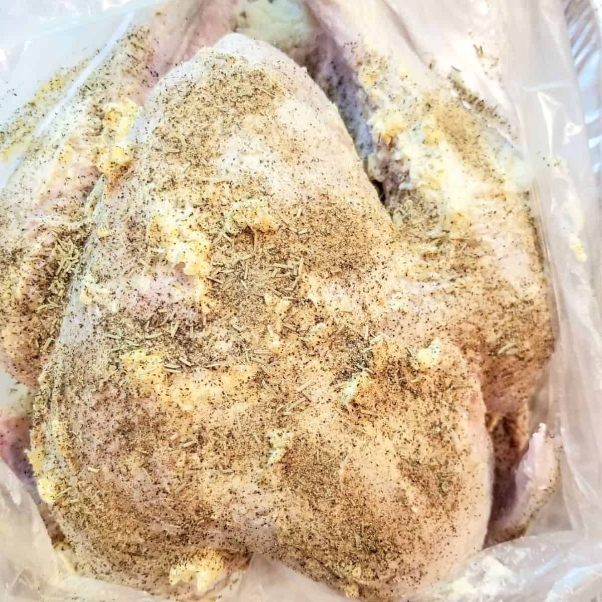 Seasoned turkey with fresh herbs and butter in a pan.
