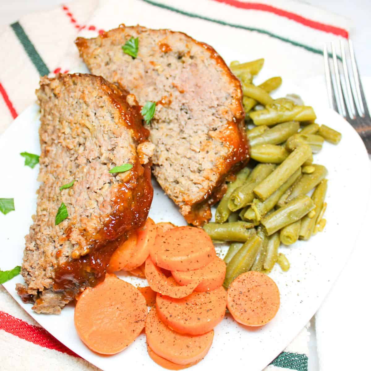 Meatloaf on a white plate with green beans and carrots.