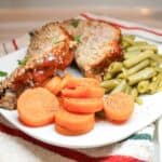 Sliced meatloaf on a white plate with green beans and carrots.