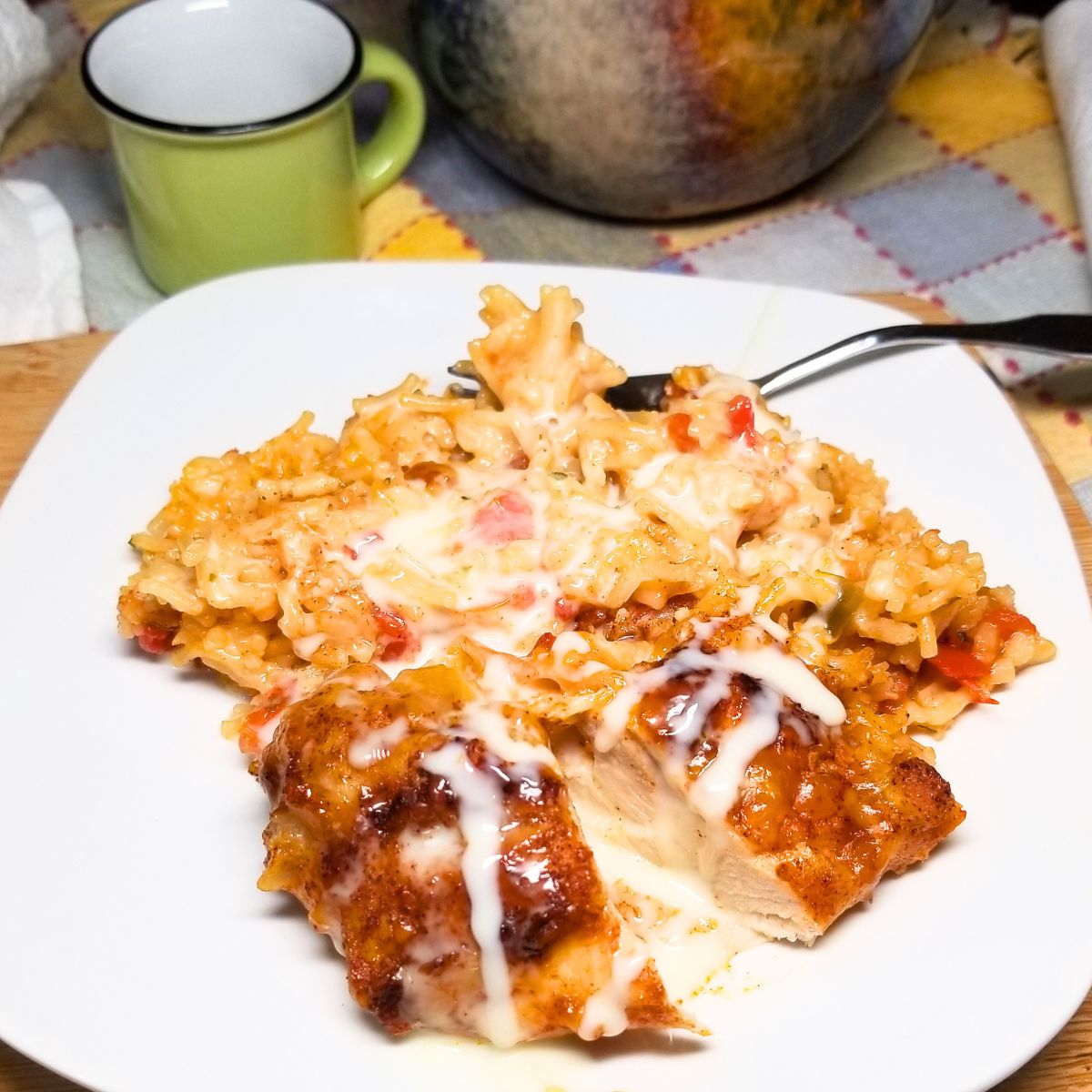 Cheesy Mexican chicken and rice topped with melted cheese and queso served on a white plate on a farmhouse table.