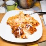 Cheesy Mexican chicken and rice topped with melted cheese and queso served on a white plate on a farmhouse table.