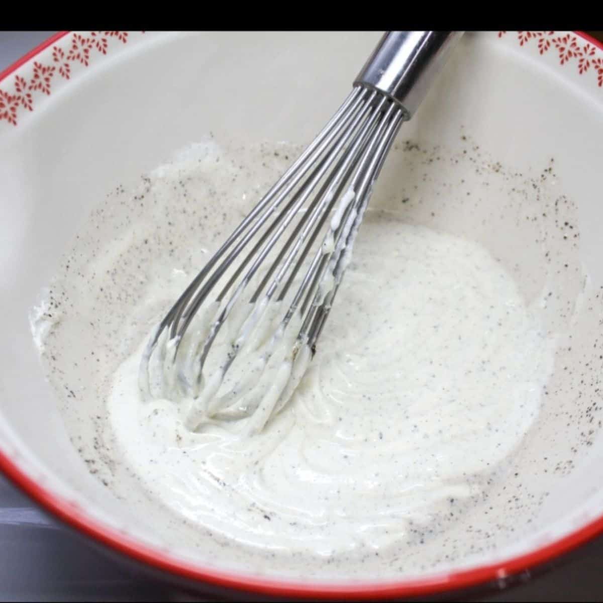 The creamy dressing mix for the pea salad in a red bowl with a whisk.