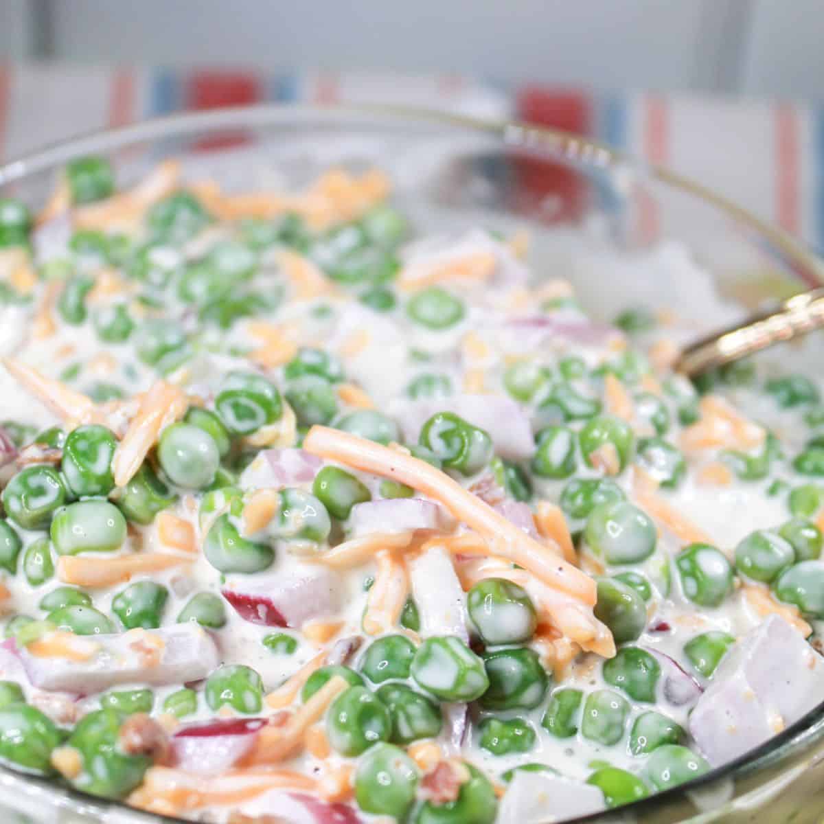 The ingredients for pea salad mixed together in a clear bowl.
