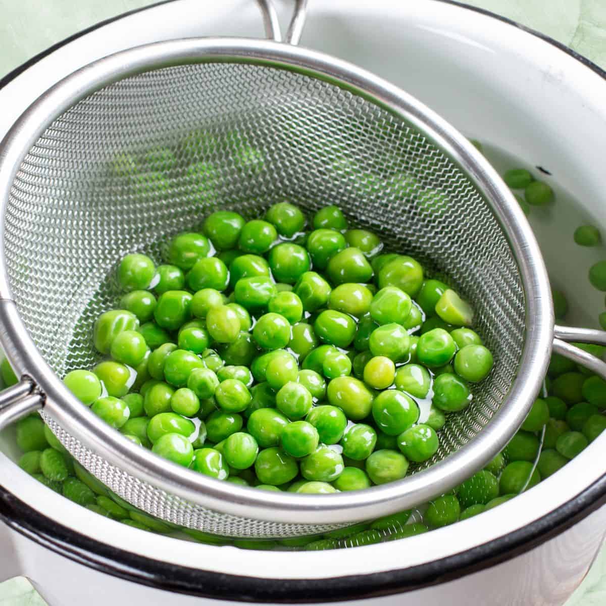 Green peas in a colander over a bowl of water.