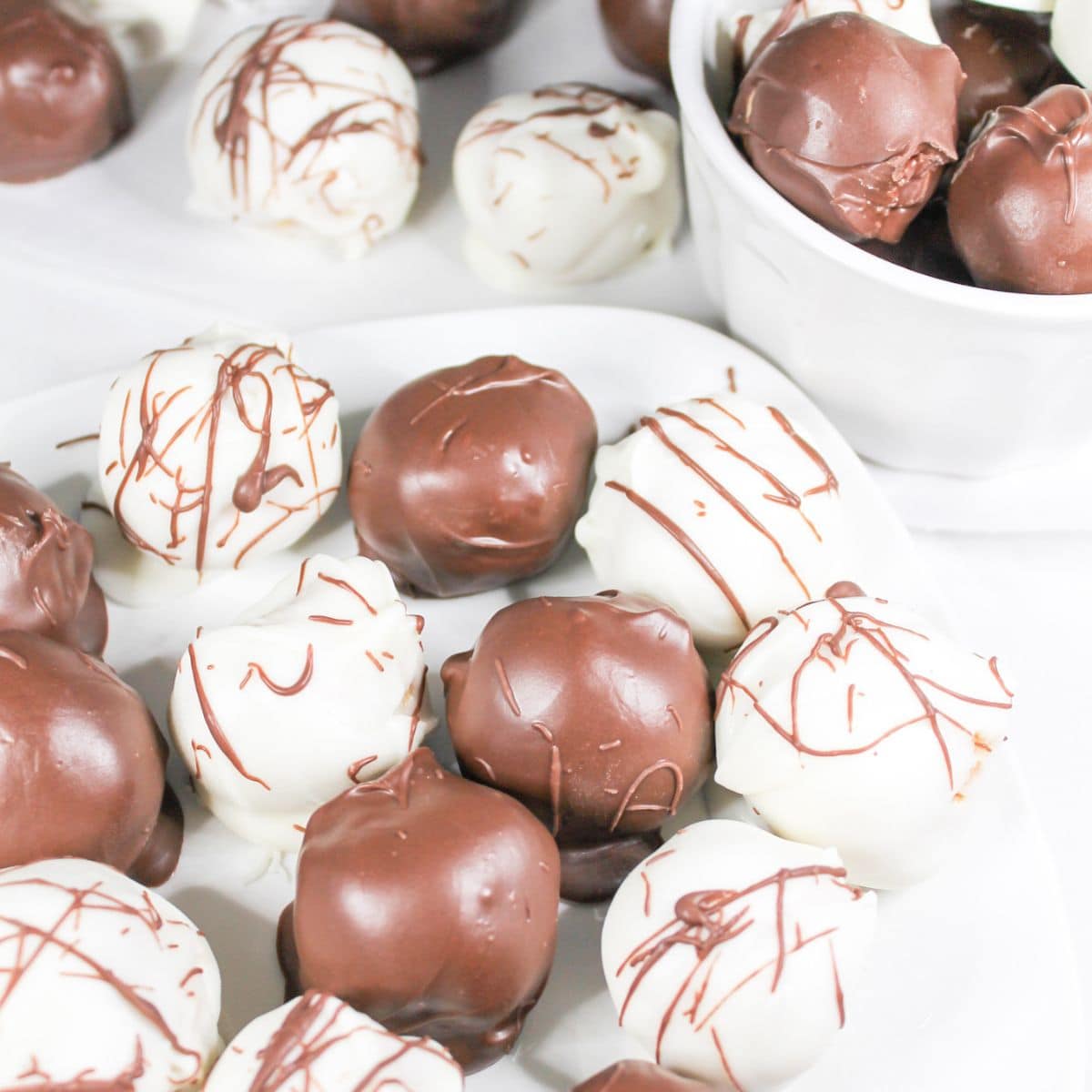 Peanut butter balls on a white serving plate, white bowl, and parchment paper.
