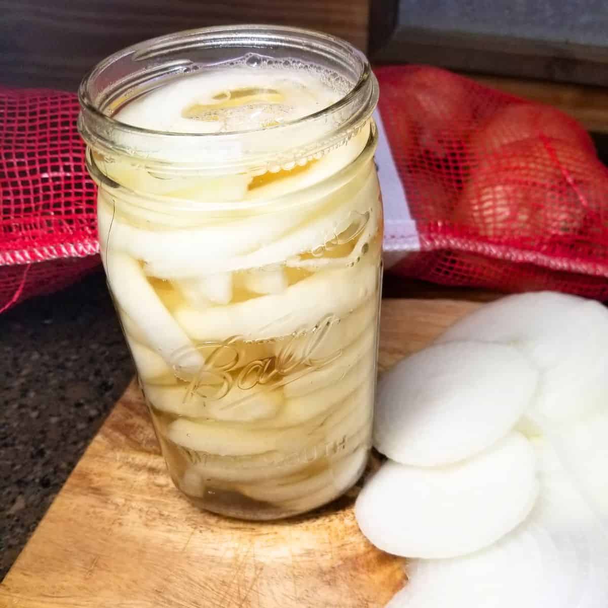 Hot pickling liquid poured over onions in a canning jar.