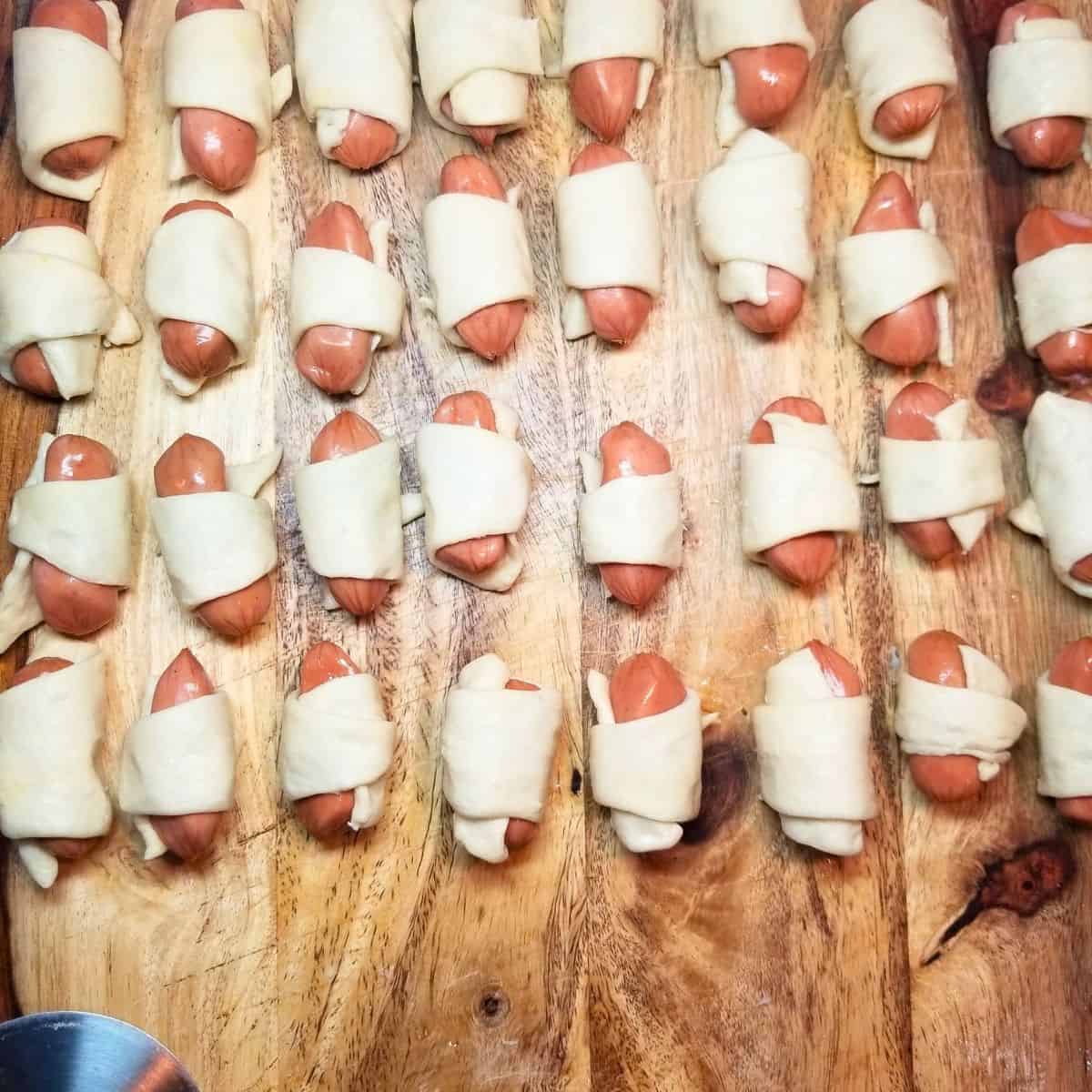 Little smokies rolled up in crescent dough to make pigs in a blanket on a cutting board.