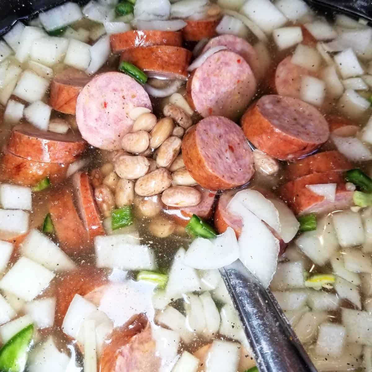 Smoked sausage rounds, diced onion, jalapeño, and garlic added to crockpot with pinto beans.