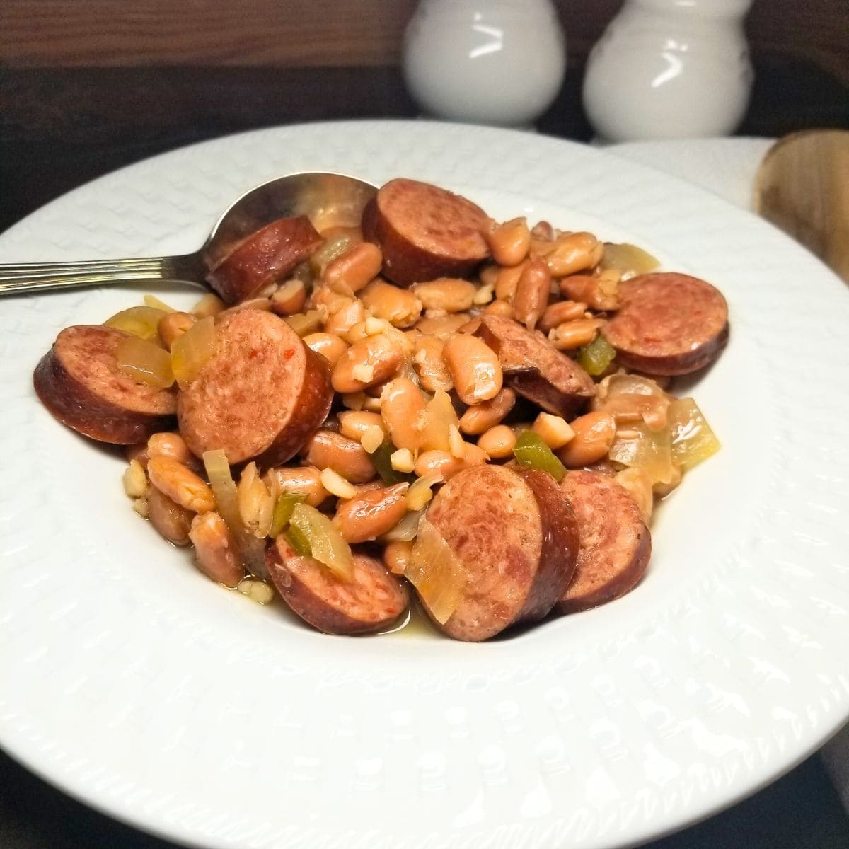 Bowl of slow cooker pinto beans and smoked sausage in a white bowl on a farmhouse table.