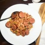 Pinto beans and sausage in a white bowl sitting on a farmhouse table.