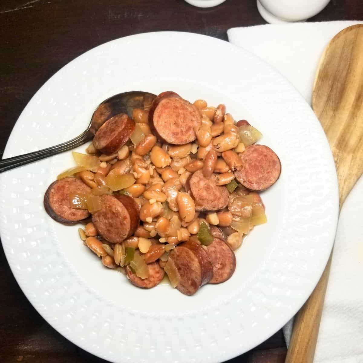 Pinto beans and sausage in a white bowl sitting on a farmhouse table.