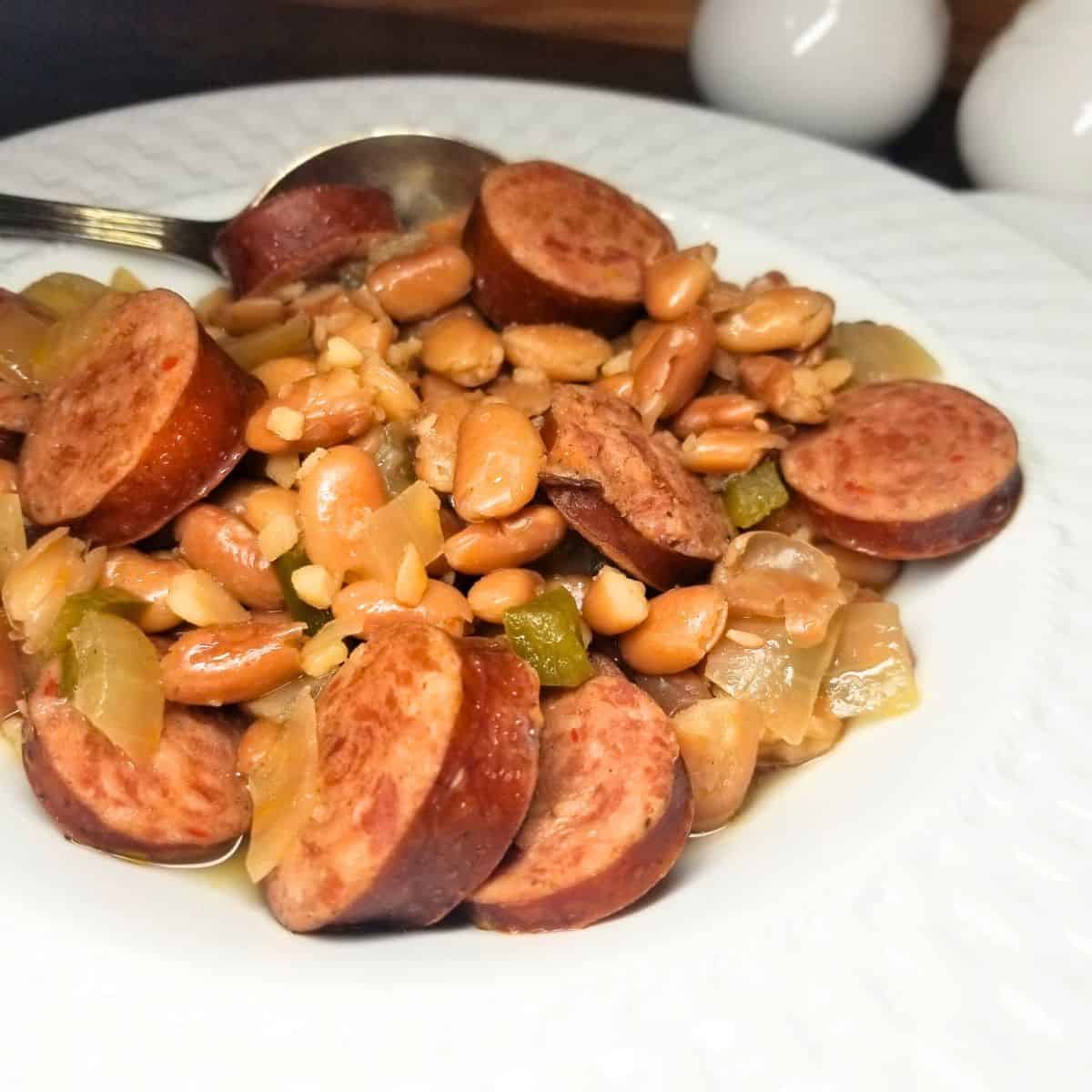 Bowl of slow cooker pinto beans and smoked sausage in a white bowl on a farmhouse table.