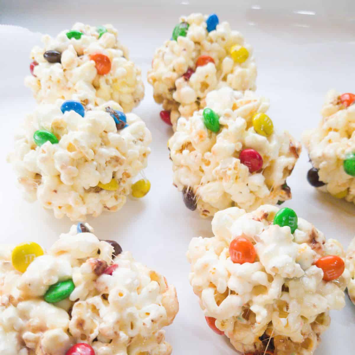 Popcorn balls with M&M's on white parchment paper.