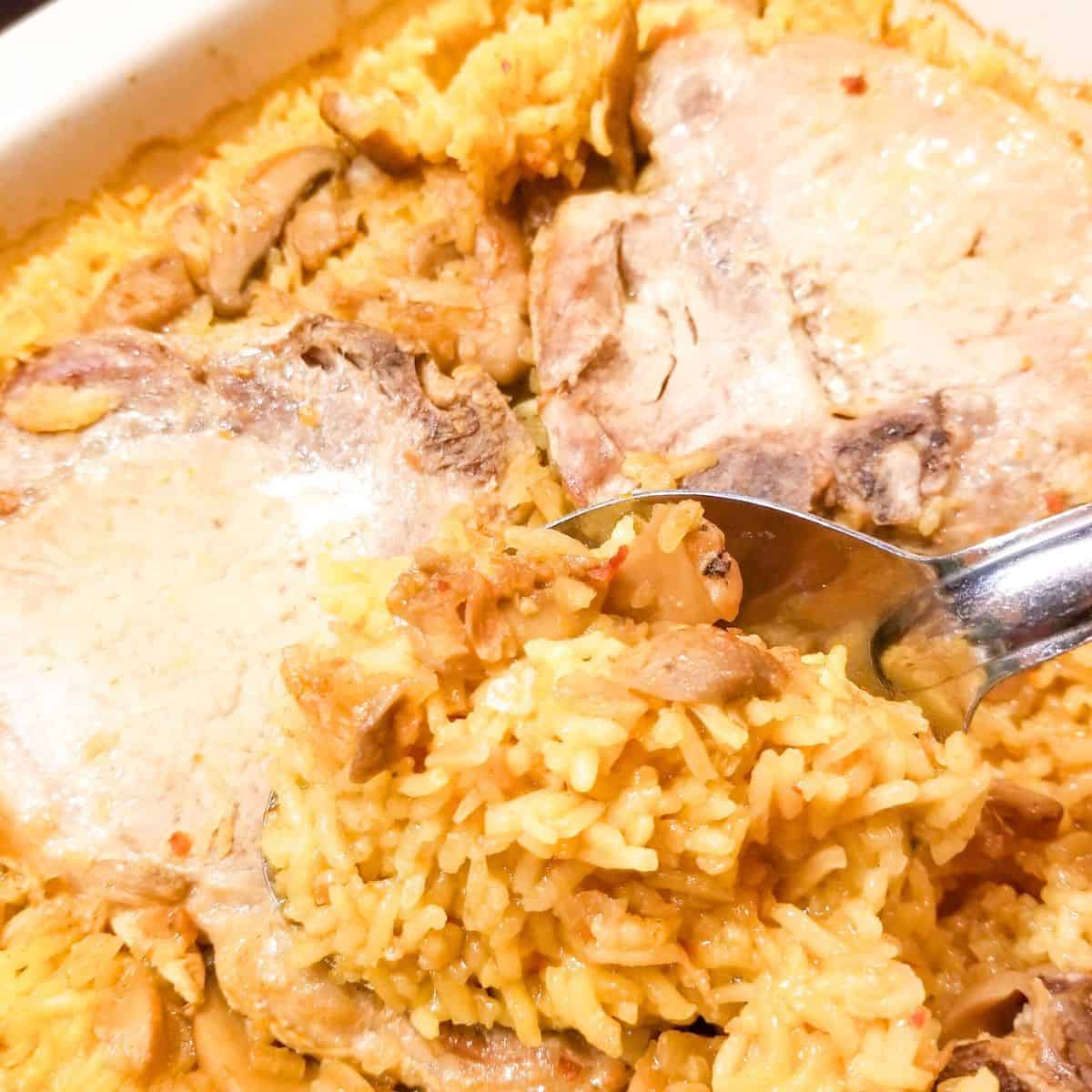 Pork chop and rice casserole in a baking dish with a spoon.