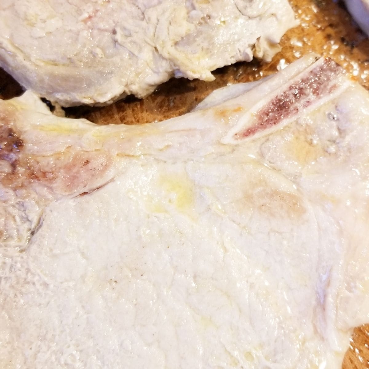 Pork chops cooking in a skillet with butter.