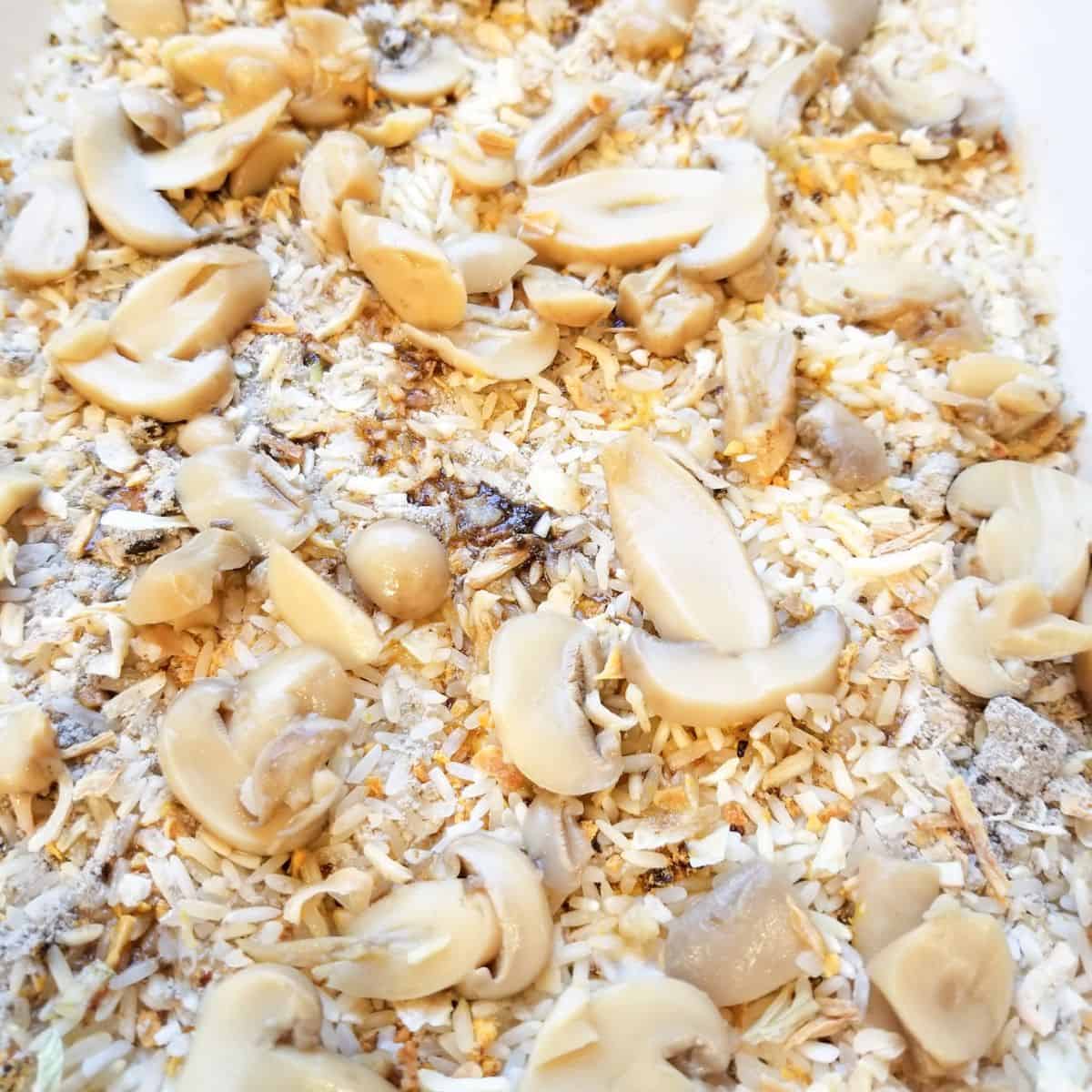 Uncooked yellow rice, onion soup mix, and mushrooms in a casserole dish.