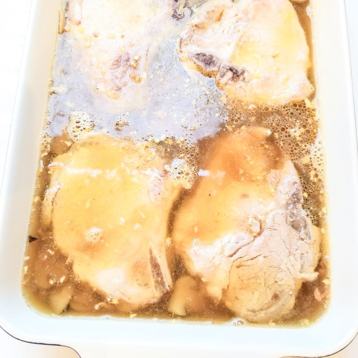Pork chops in a casserole dish with the ingredients ready to bake.