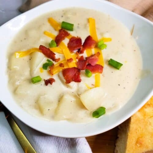 Potato soup in a white bowl topped with bacon, cheese, and green onions.