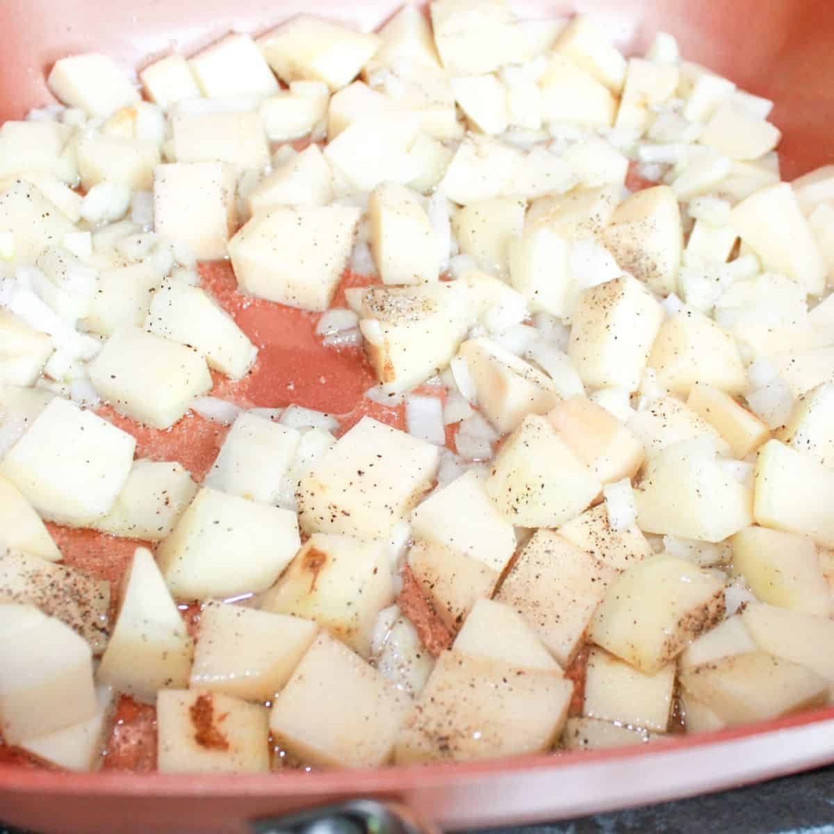 Seasoned potatoes and onions in a skillet on the stovetop.