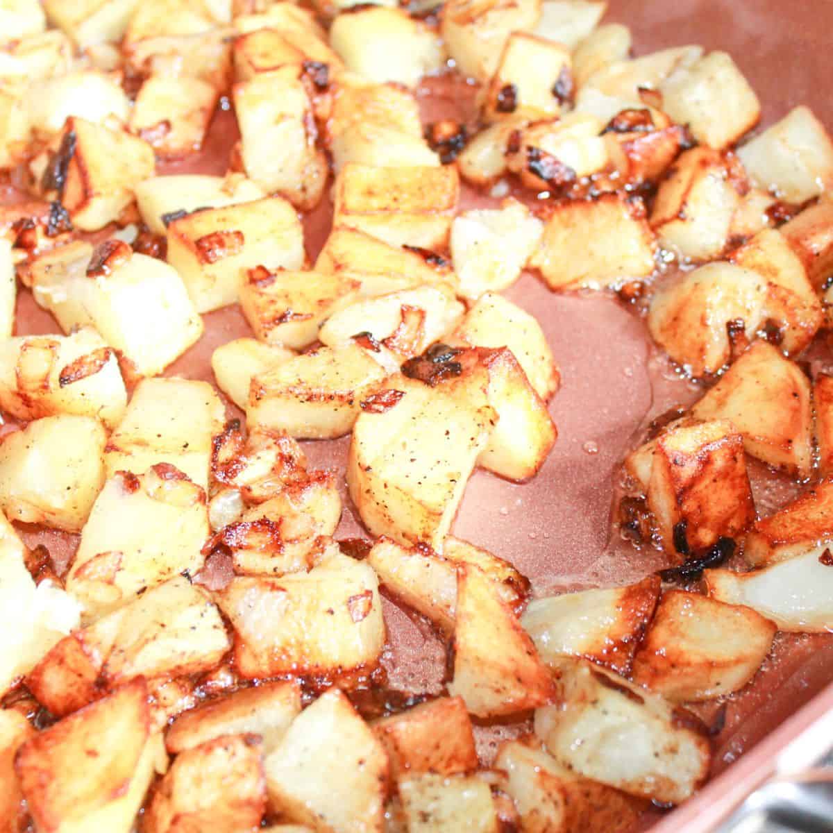 Frying potatoes and onions in a skillet until browned.