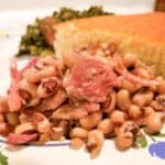 Slow cooker purple hull peas on a plate with cornbread and greens.