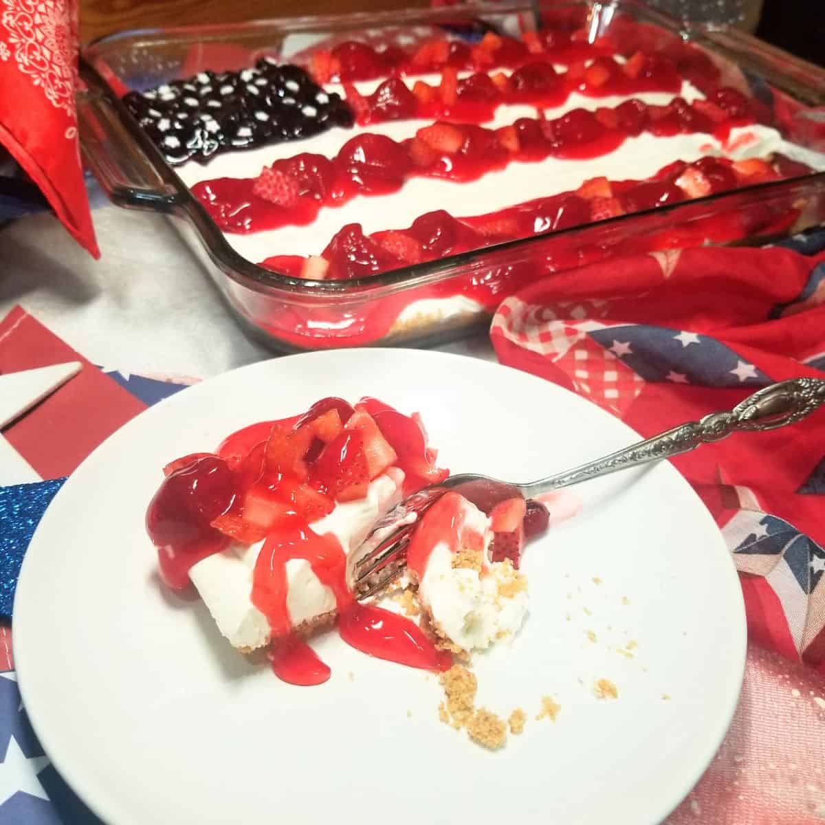 American Flag Cheesecake garnished with fresh strawberries, blueberries on top of pie filling and a slice of cheesecake on a plate.