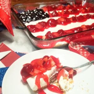 American Flag Cheesecake garnished with fresh strawberries, blueberries on top of pie filling and a slice of cheesecake on a plate.