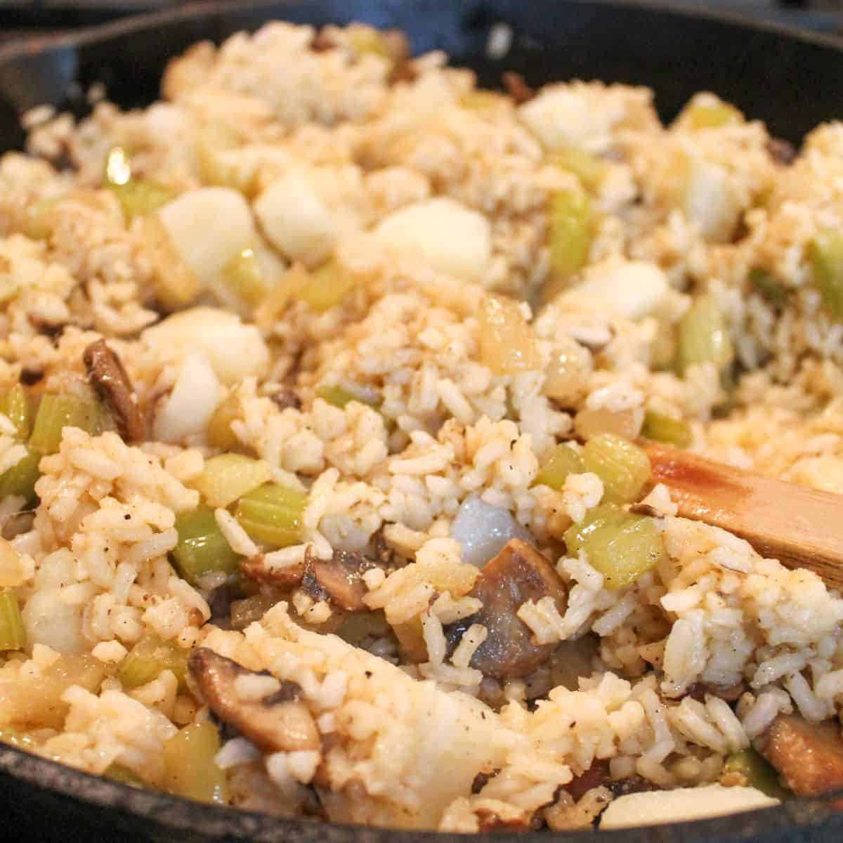 Rice dressing in a black skillet with a wooden spoon.