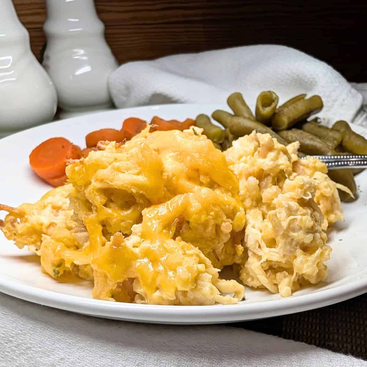Chicken Rice-A-Roni Casserole with shredded chicken, creamy sauce, and melted cheese on a white plate with green beans and carrots.