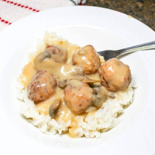 Meatballs and gravy over rice in a white bowl with a fork.