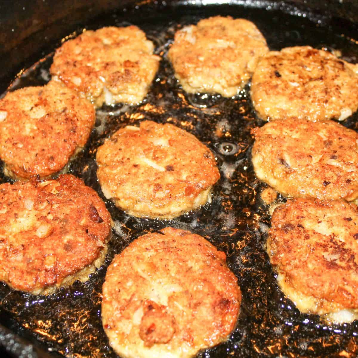 Salmon patties cooking in a cast iron skillet.